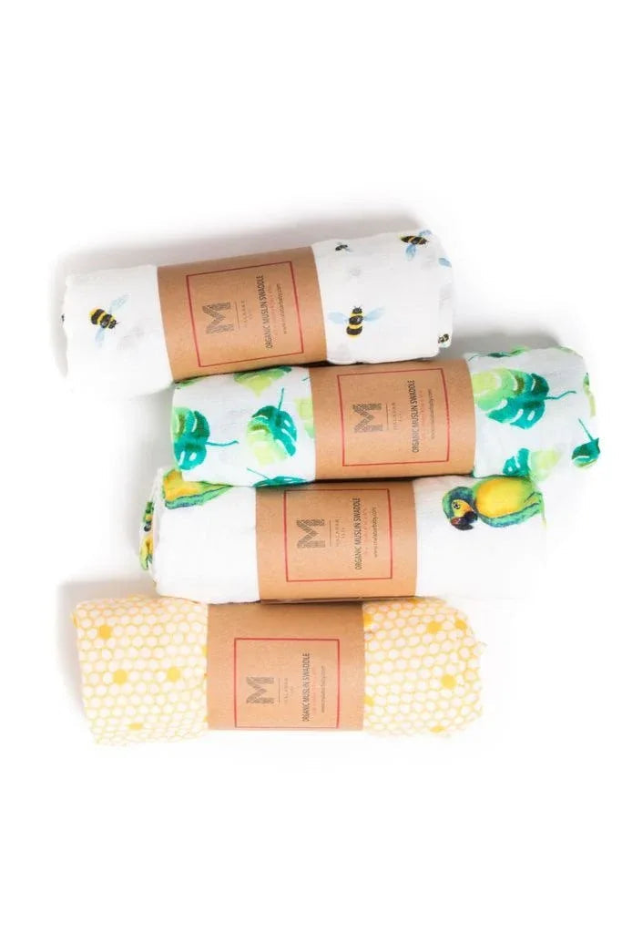 Four pastel watercolor printed muslin baby swaddles arranged on a tropical leaf background.