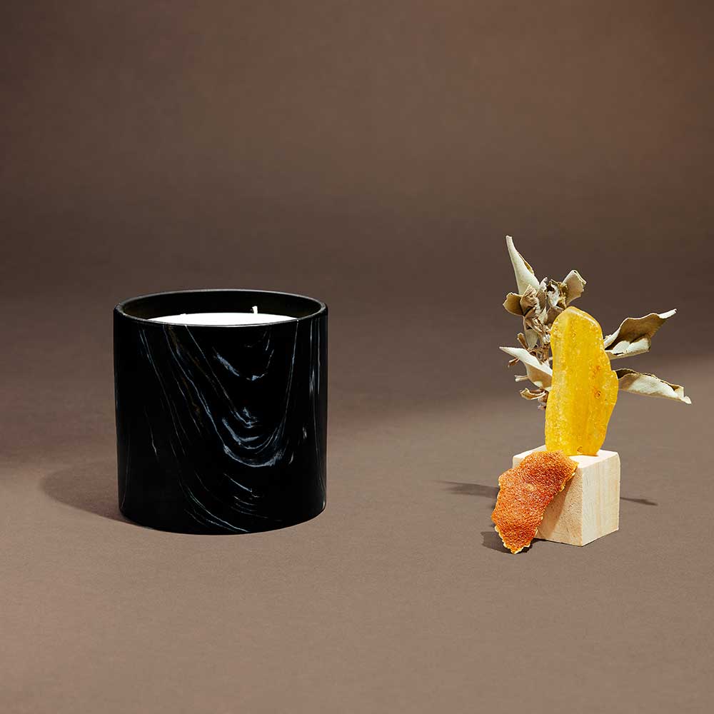 Close-up of elegant black Marquina ceramic vessel with white and gold swirls, unlit candle.