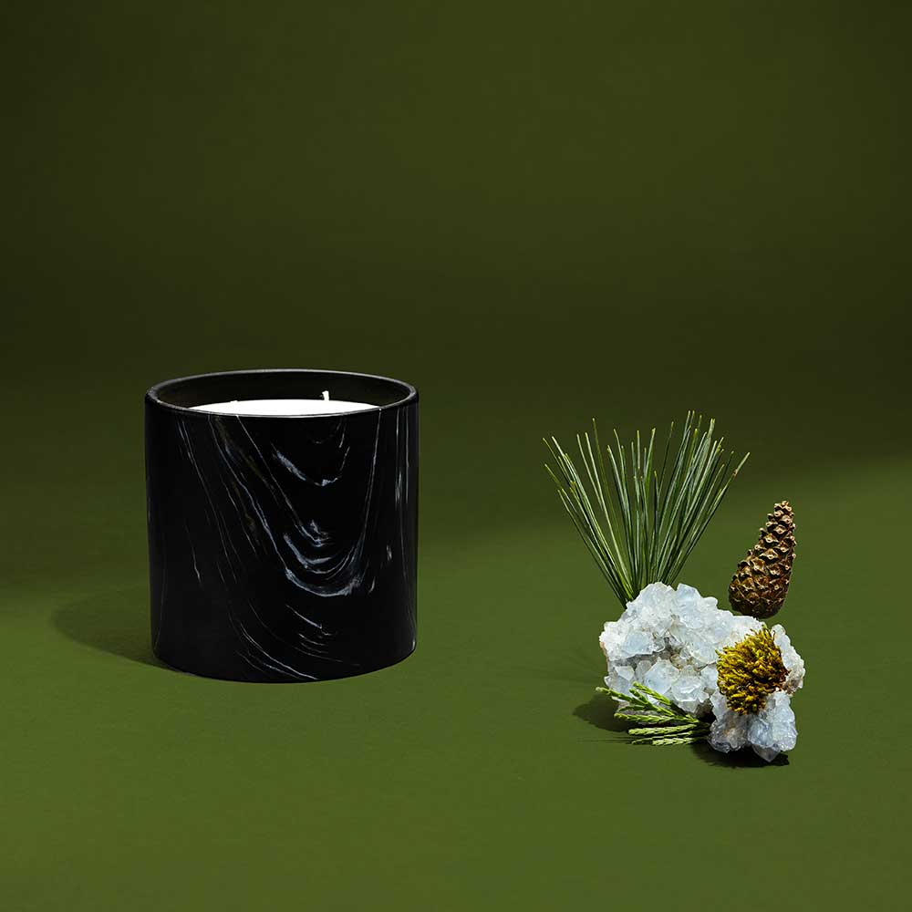 Close-up of black ceramic candle holder with white and gold marquina design, featuring evergreen pine cones.