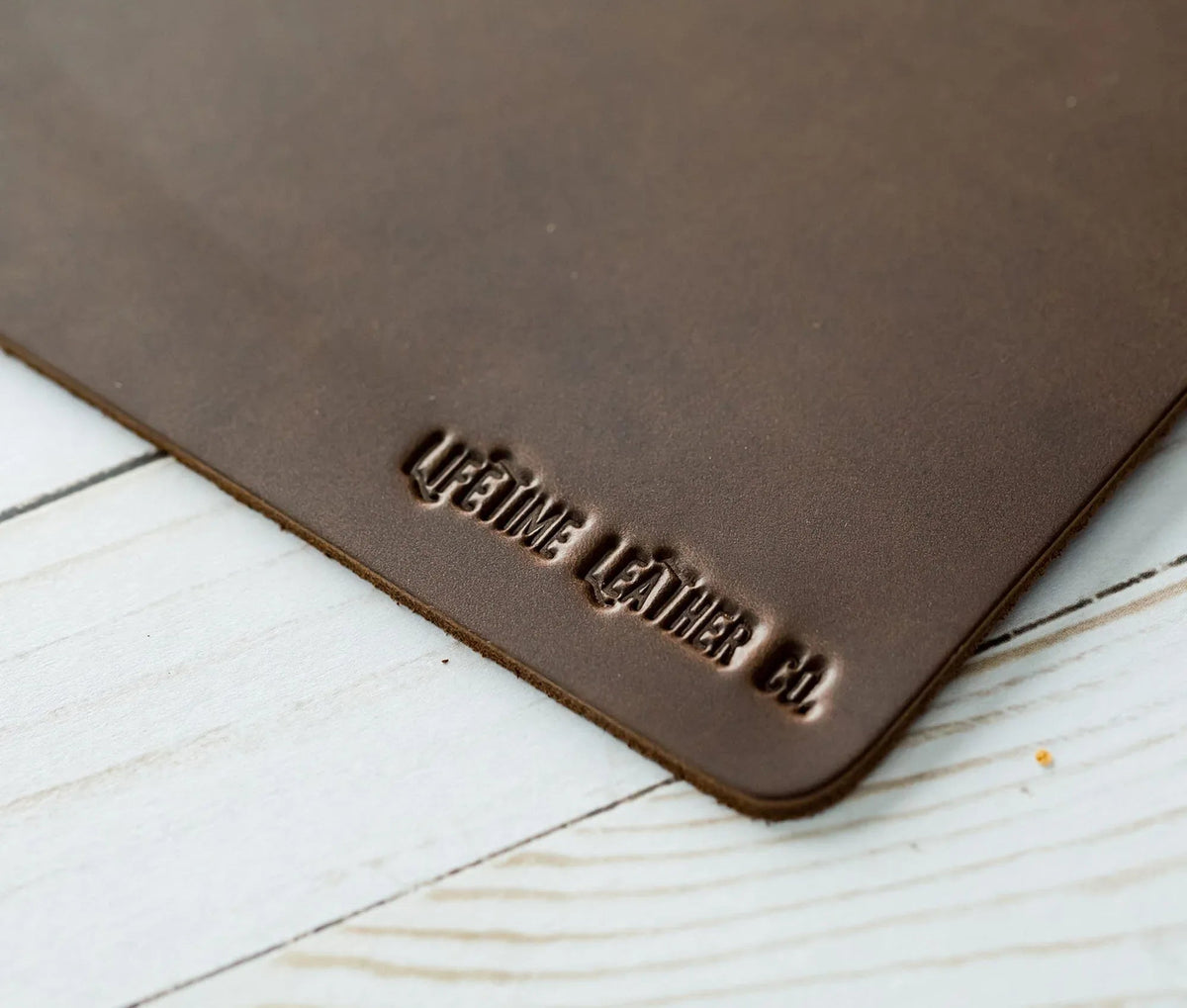 Close-up view of corner of dark brown leather mouse pad showing texture and thickness.