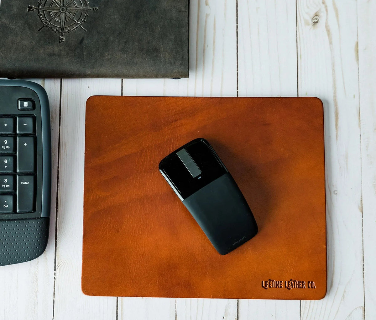 Leather mouse pad placed on wooden desk under computer mouse in office setup.