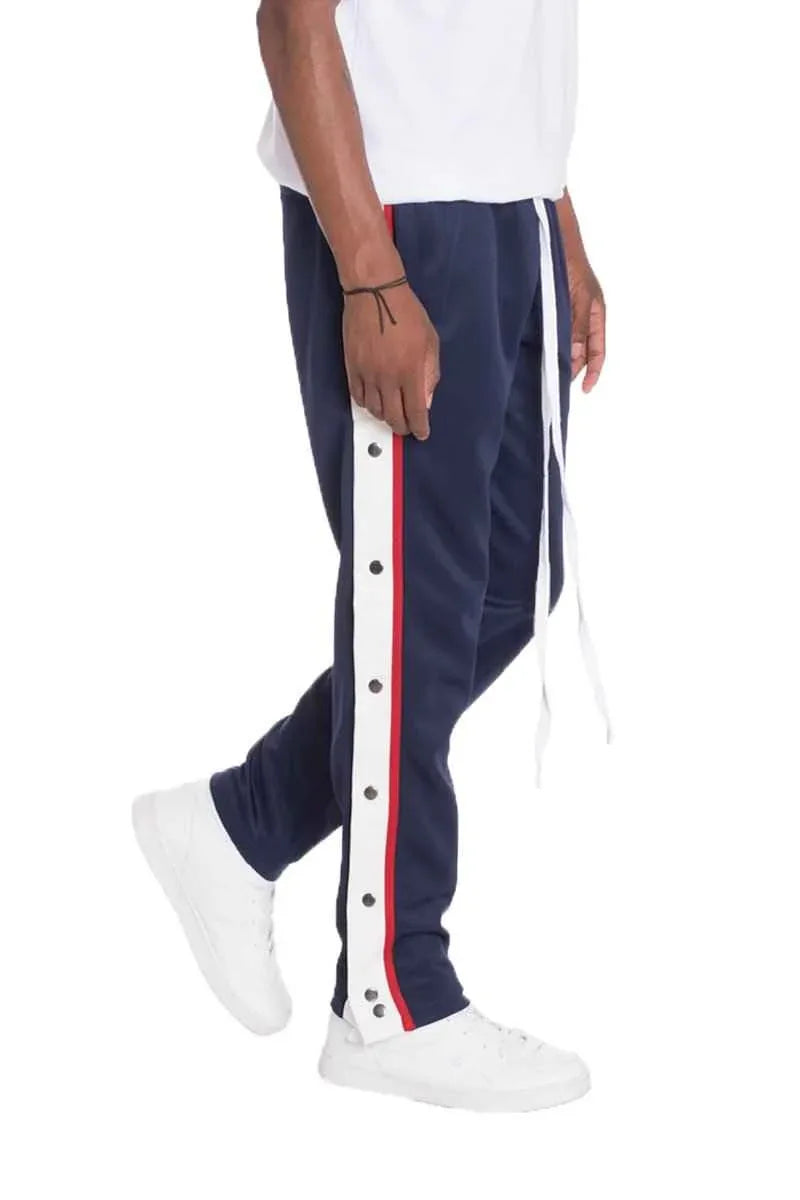 Front view of navy snap button track pants with snap closures down the sides worn by a model.