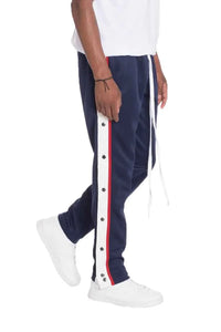 Front view of navy snap button track pants with snap closures down the sides worn by a model.