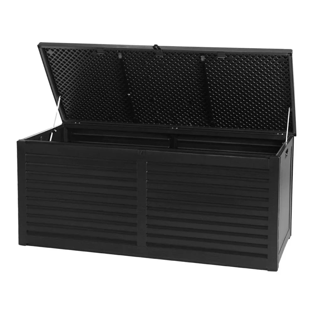 Black outdoor storage box with wood-texture finish placed on a patio beside plants.
