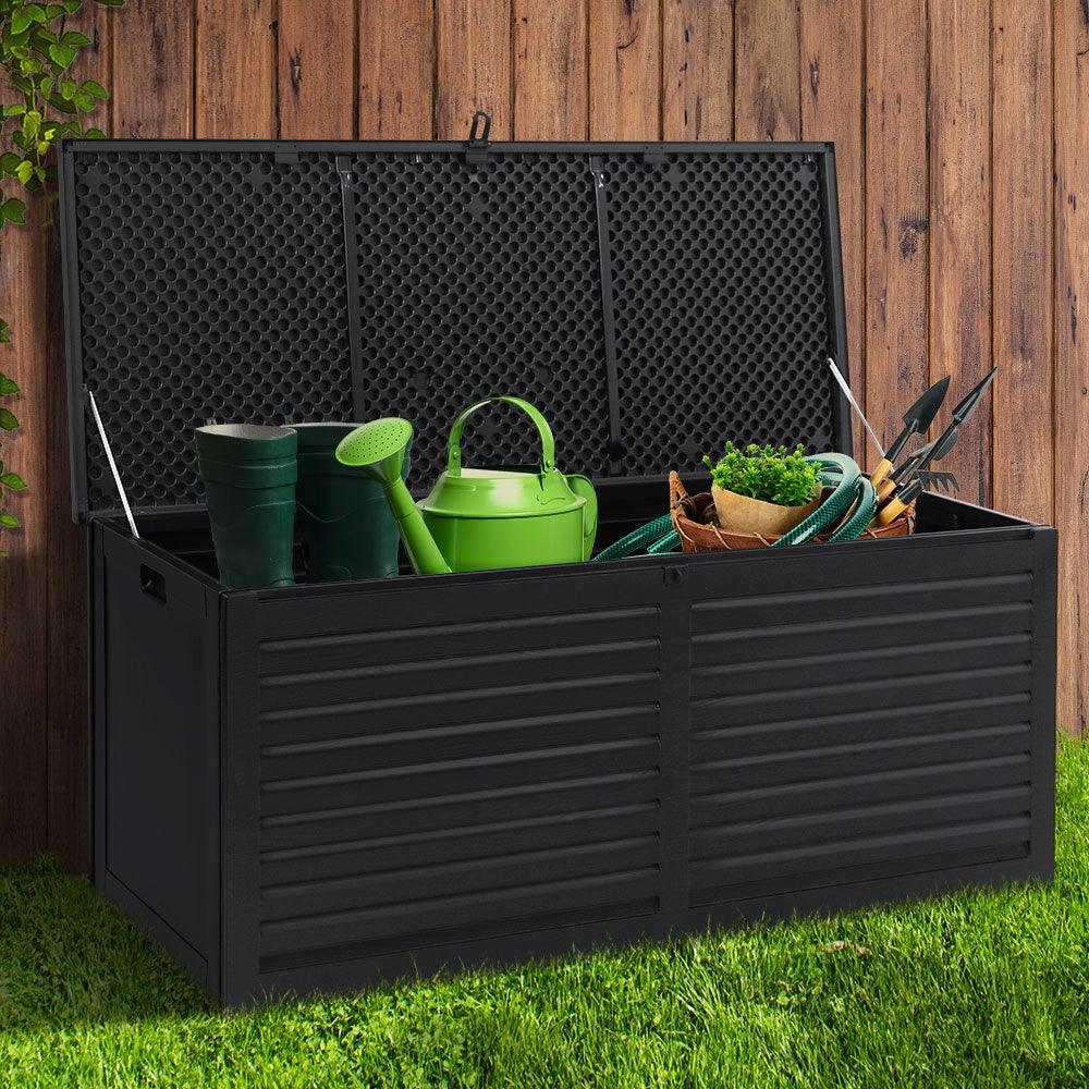 Black storage box closed on patio, surrounded by greenery and outdoor furniture.