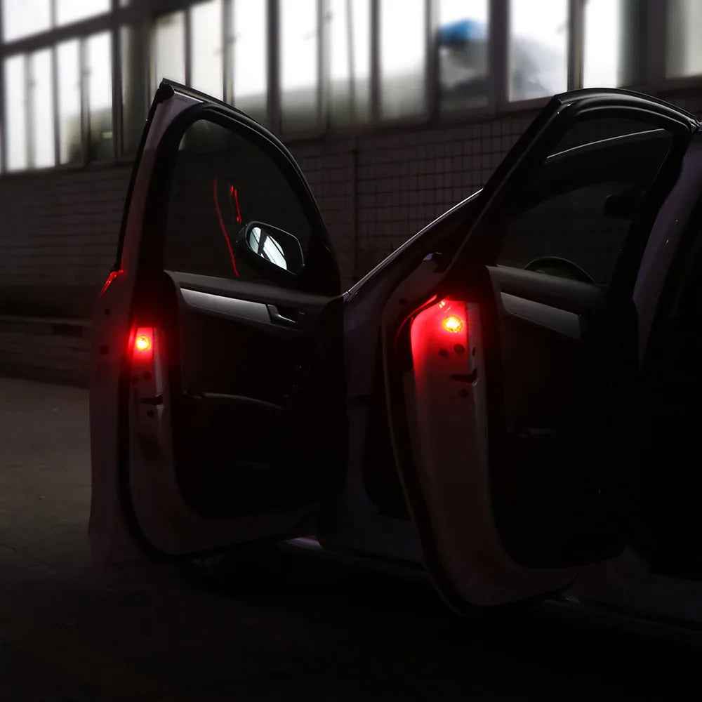 A pair of small, round wireless car door warning lights glowing red on an open car door at night.