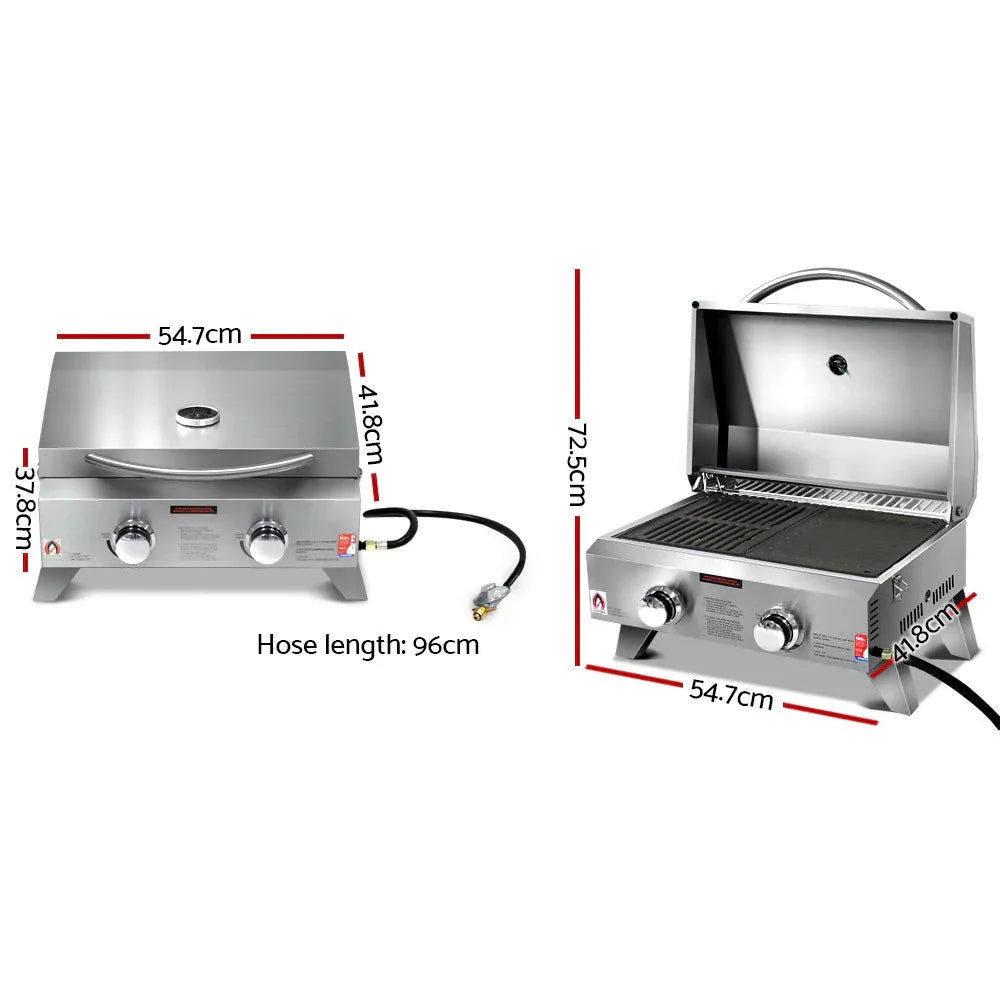 Portable gas BBQ grill opened showing two burners, side handles, and integrated thermometer on lid.