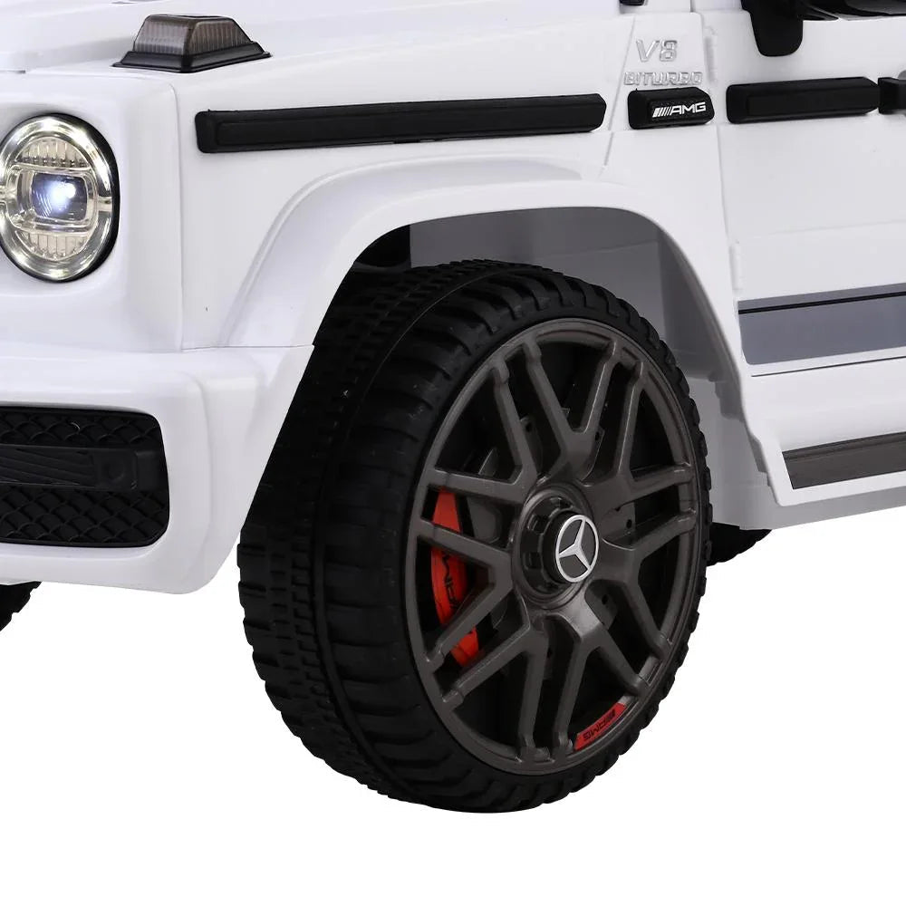 Remote control held in hand to operate white Mercedes-Benz AMG G63 kids ride-on car