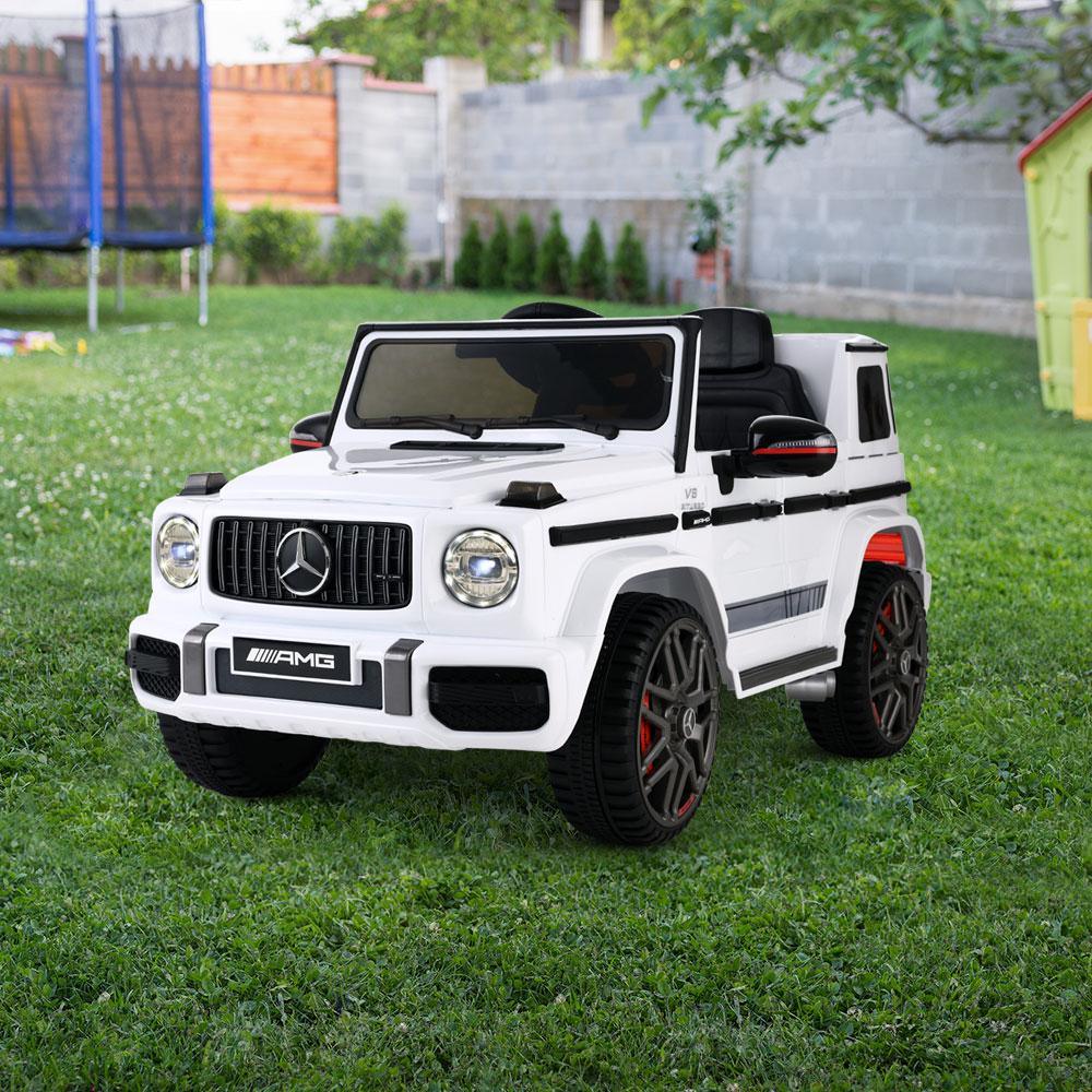 White AMG G63 kids ride-on car with doors open and remote control beside it