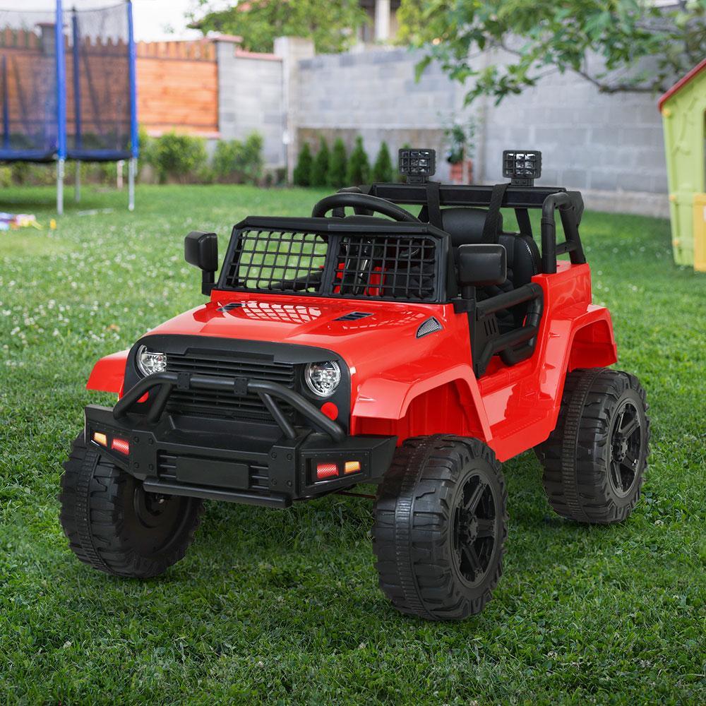 Side view of red kid’s electric jeep with parent using remote control nearby.