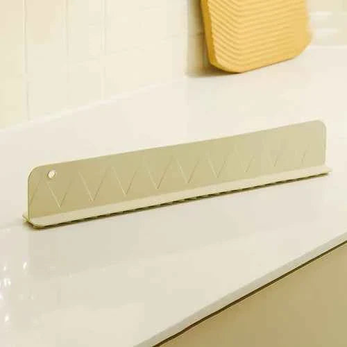 Gray silicone sink splash guard with suction cups attached, placed along a kitchen sink edge to prevent water splashing.