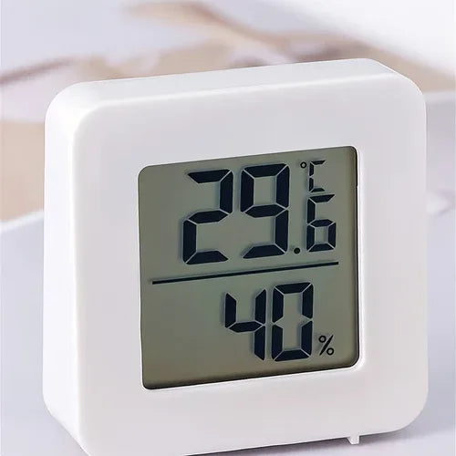 Modern temperature and humidity meter standing upright on smooth surface, showing digital readings.