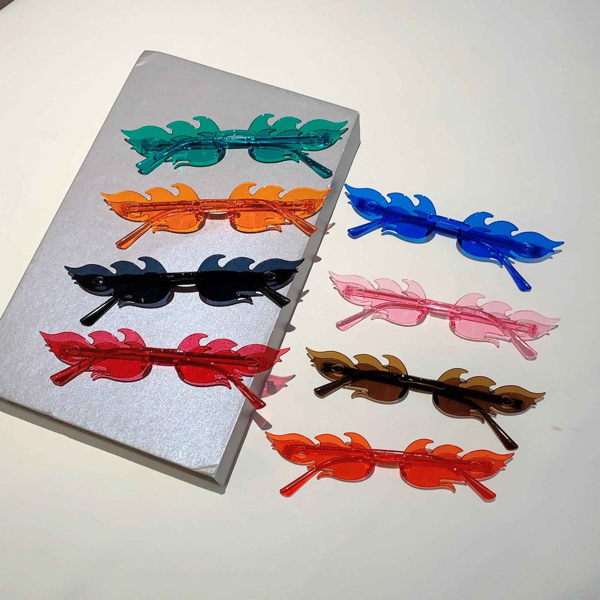 Set of twelve flame-shaped sunglasses in vibrant colors, arranged stylishly on a white background.