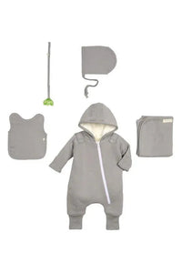Baby dressed in gray jumpsuit with feet covers, lying on a white blanket.
