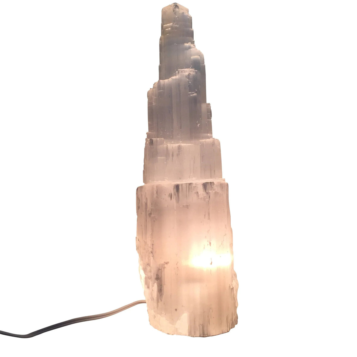 Tall selenite crystal lamp shaped like a skyscraper emitting soft white light on a white surface.