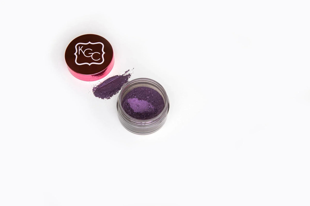 Close-up of Sugar Hill Shimmer Powder with bold eggplant color in small jar on white background.