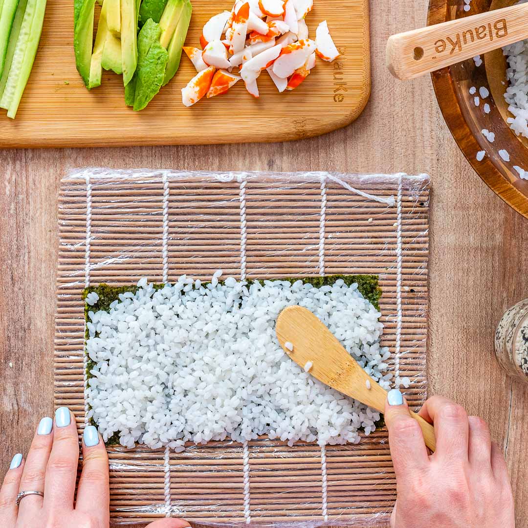 Bamboo sushi making tools such as rolling mats, chopsticks, and rice spreaders on a dark wooden table.