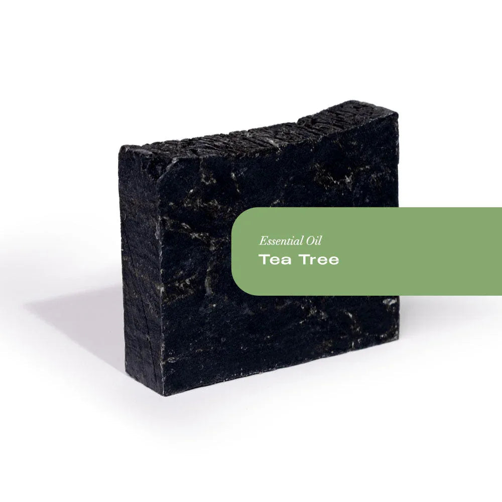 Rectangular bar of black tea tree activated charcoal organic soap with white label on wood background.