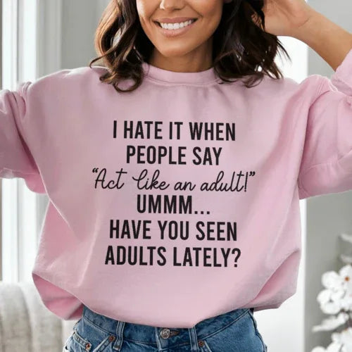 Light pink sweatshirt with 'Act Like An Adult' phrase in soft peach text, showing fleece's warm and cozy texture.