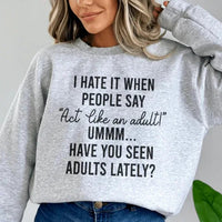 Close-up of sport grey sweatshirt detailing 'Act Like An Adult' peach text with adjustable cuffs and soft fleece inside.