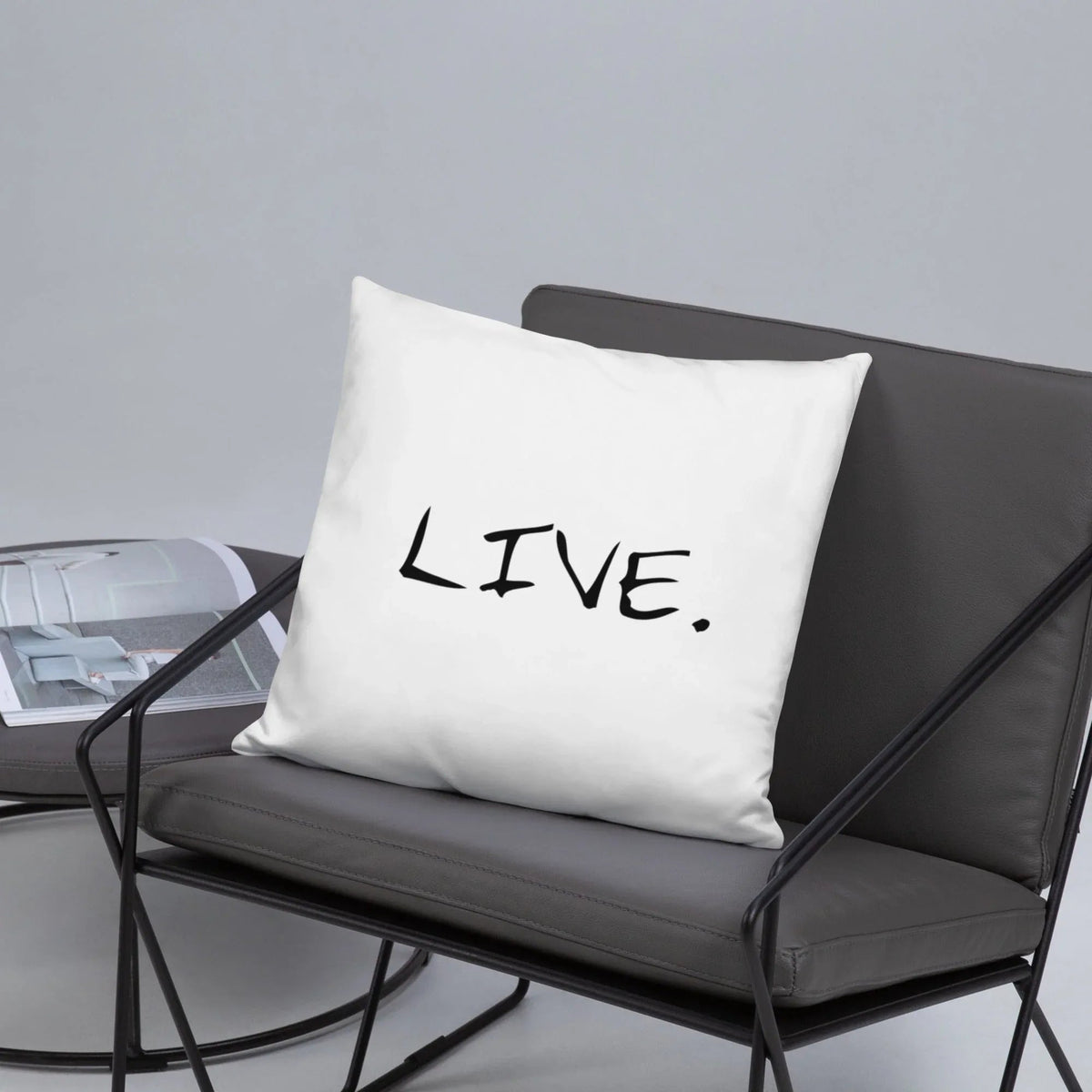 White pillow on a grey armchair beside a large plant in a modern room setting