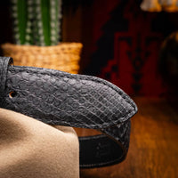 Person seated wearing Arkansas black python belt paired with dark denim and leather boots