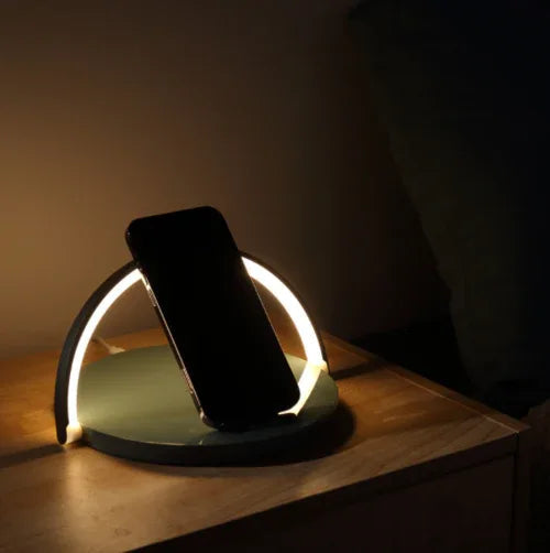 A sleek black wireless charging block holds a smartphone upright on a wooden desk, charging the device.