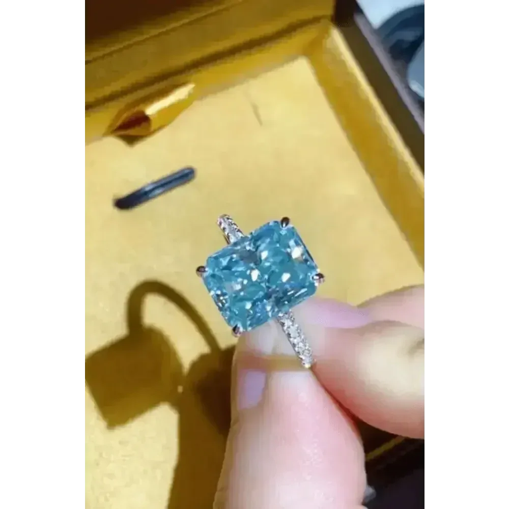 Ring held between fingers highlighting blue gemstone brilliance