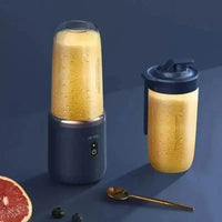 Juicer cup in blue with a clear blending jar filled with mixed fruits on a table.