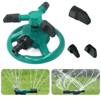 Green garden sprinkler spraying water over grass in outdoor setting.