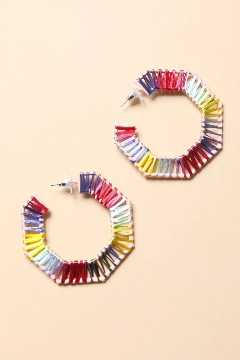 Side view of colorful raffia hoop earrings showcasing bold colors and woven detail on a plain background.