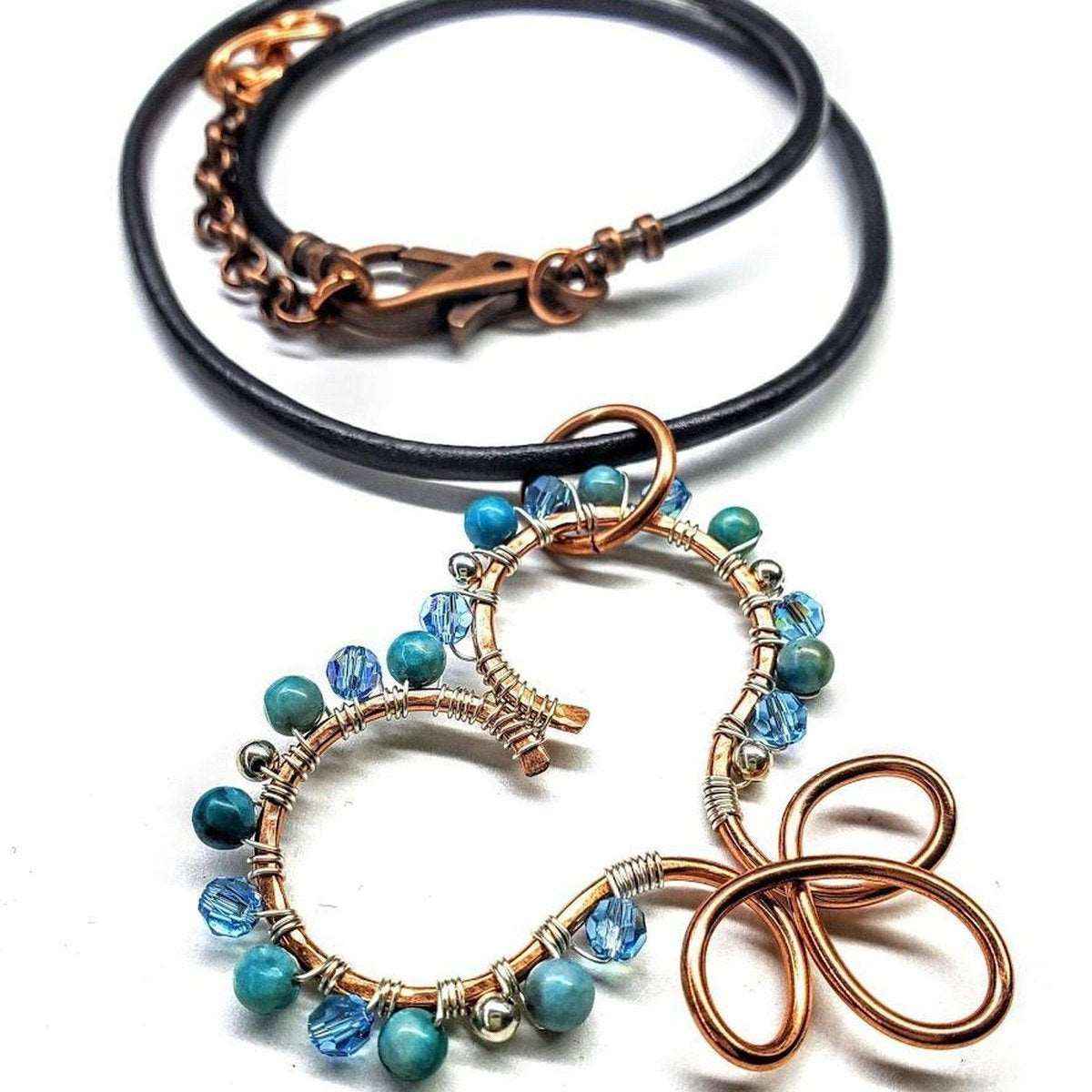 Close view of wire sculpted copper heart pendant featuring turquoise and silver beads on leather necklace.
