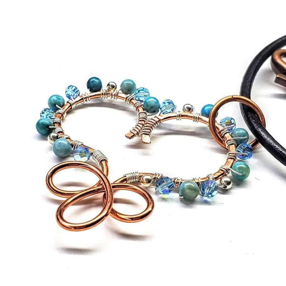 Detailed view of copper heart pendant featuring turquoise beads and silver accents on brown leather necklace.