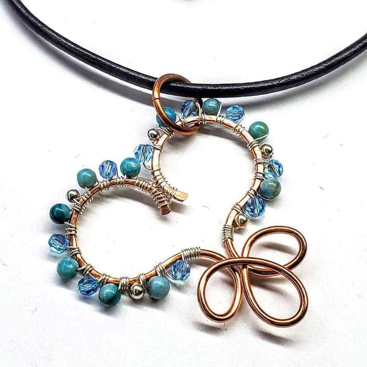 Close-up of handcrafted copper wire heart pendant with turquoise, silver, and crystal beads on leather necklace.