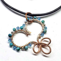 Close-up of handcrafted copper wire heart pendant with turquoise, silver, and crystal beads on leather necklace.