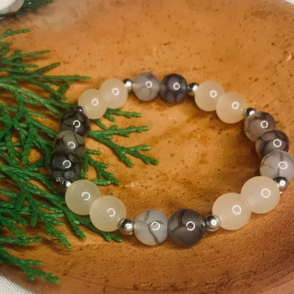 Close-up of natural gray and white agate gemstone beads with silver spacers on elastic bracelet.