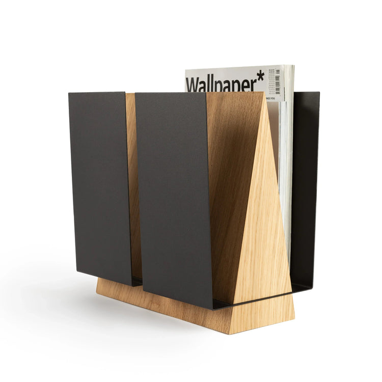 Standing magazine holder WINGS in oak wood and black metal with magazines arranged inside on a wooden floor.