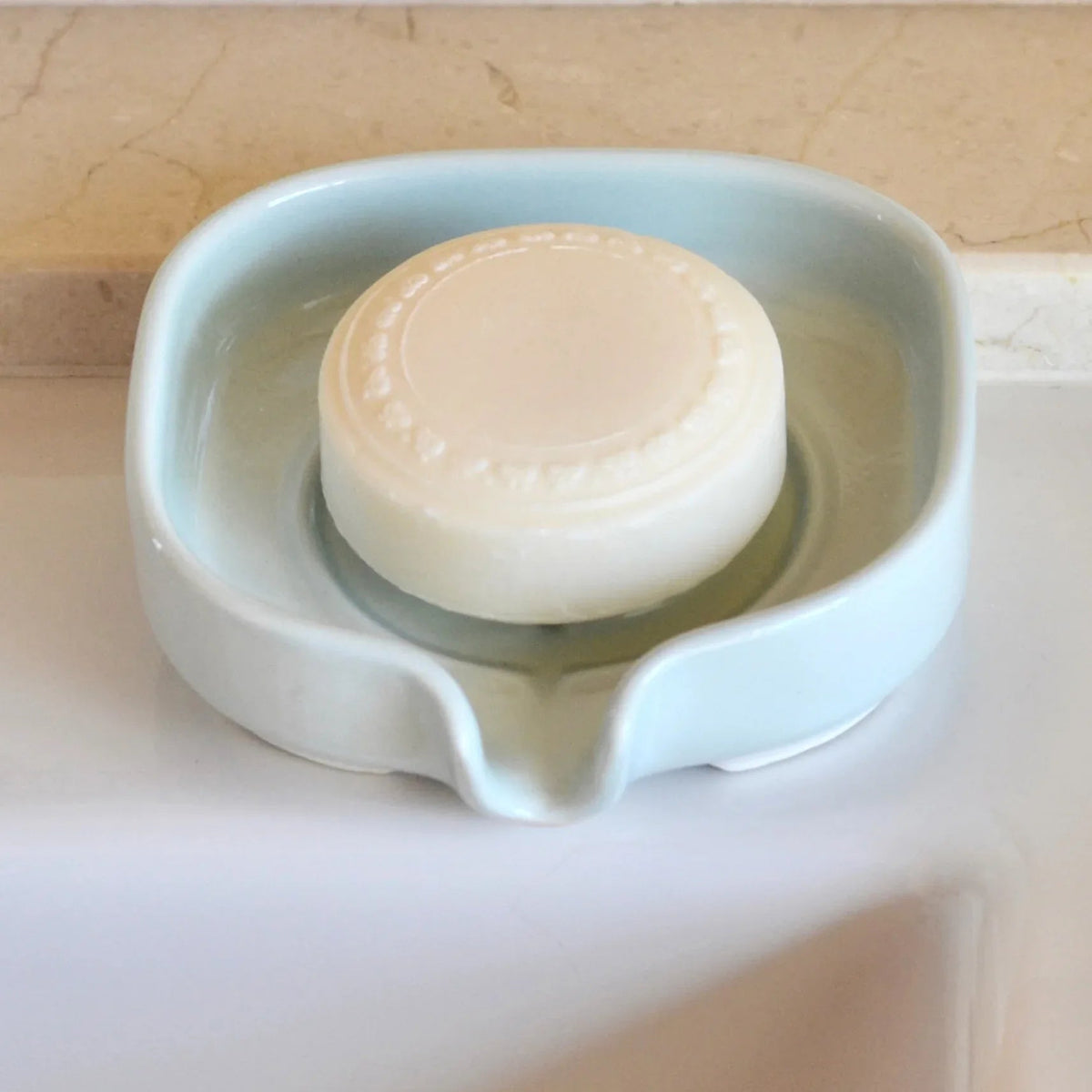 Top-down view of white porcelain soap dish with drainage slots on wooden bathroom counter.