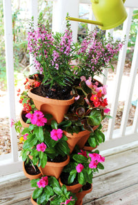 Stacking planters hung by chains filled with vibrant flowers on a wooden exterior wall.