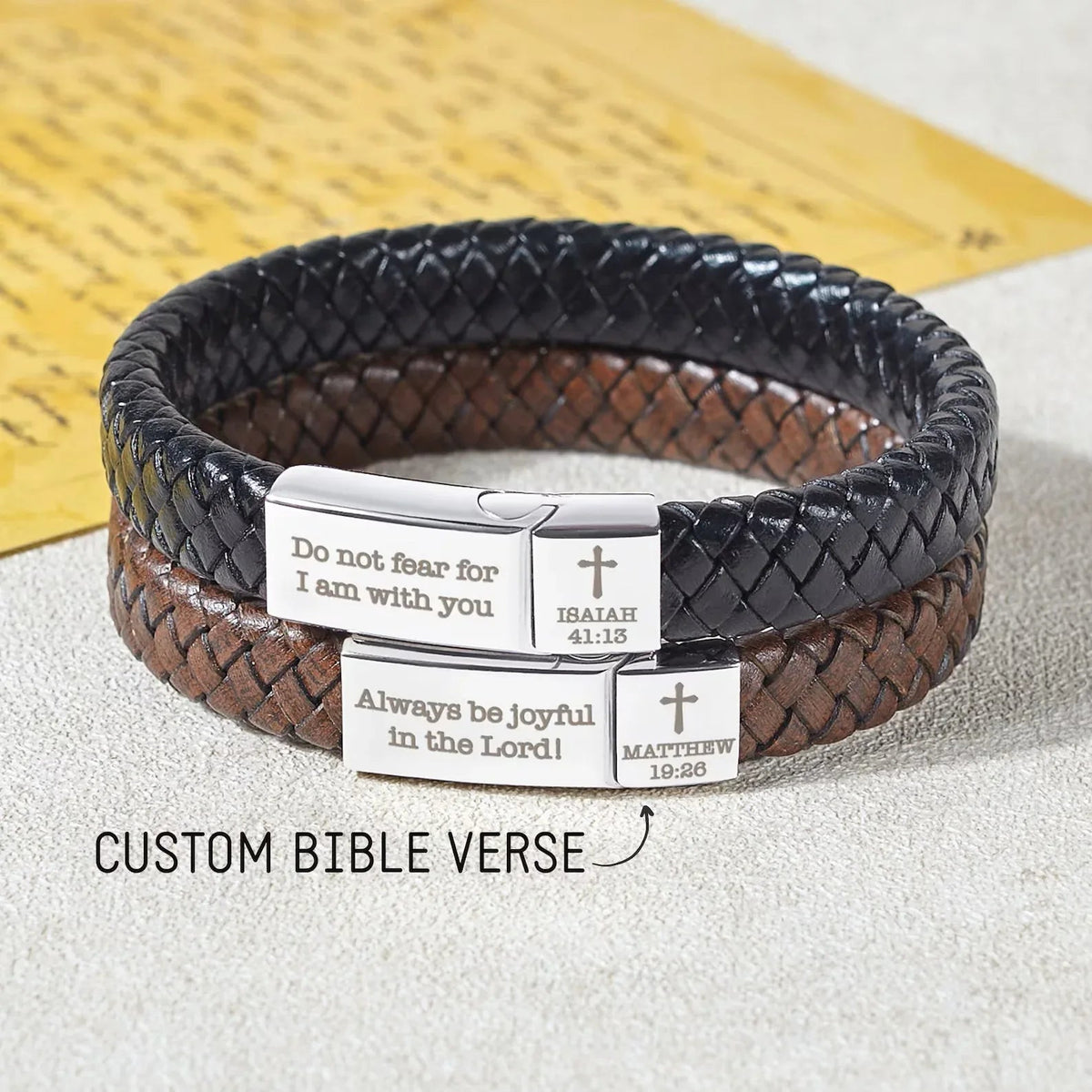 Close-up of woven leather Christian bracelet with stainless steel cross and Bible quote engraving.