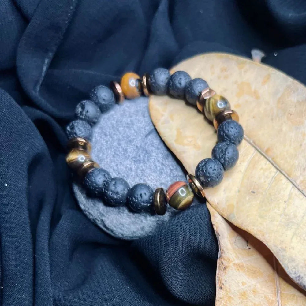 Beaded bracelet made of black lava stones, Tiger Eye gemstones, and copper spacer beads on white.