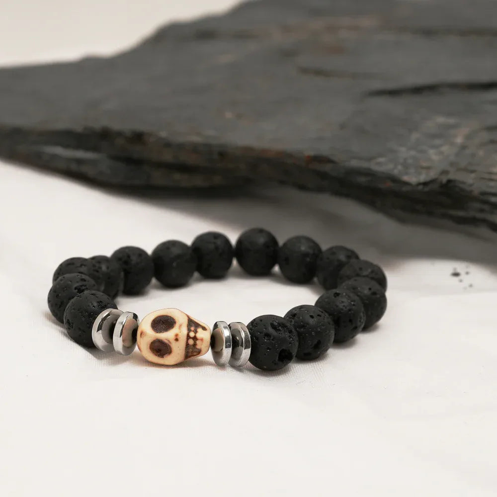 Close-up of black lava stone bracelet with silver spacers and central skull bead on dark background