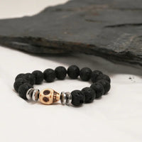Close-up of black lava stone bracelet with silver spacers and central skull bead on dark background