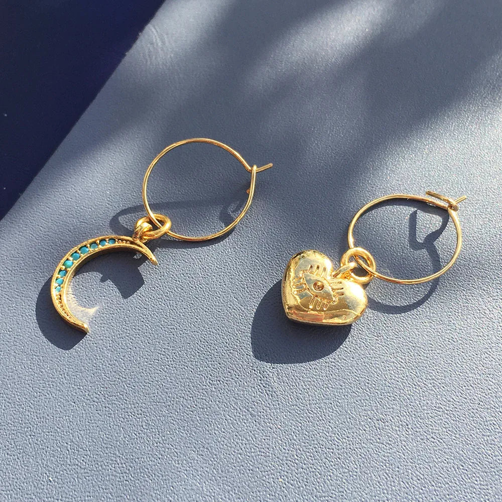 Detailed view of gold plated mini hoops with turquoise crystal moon and chunky heart charms.