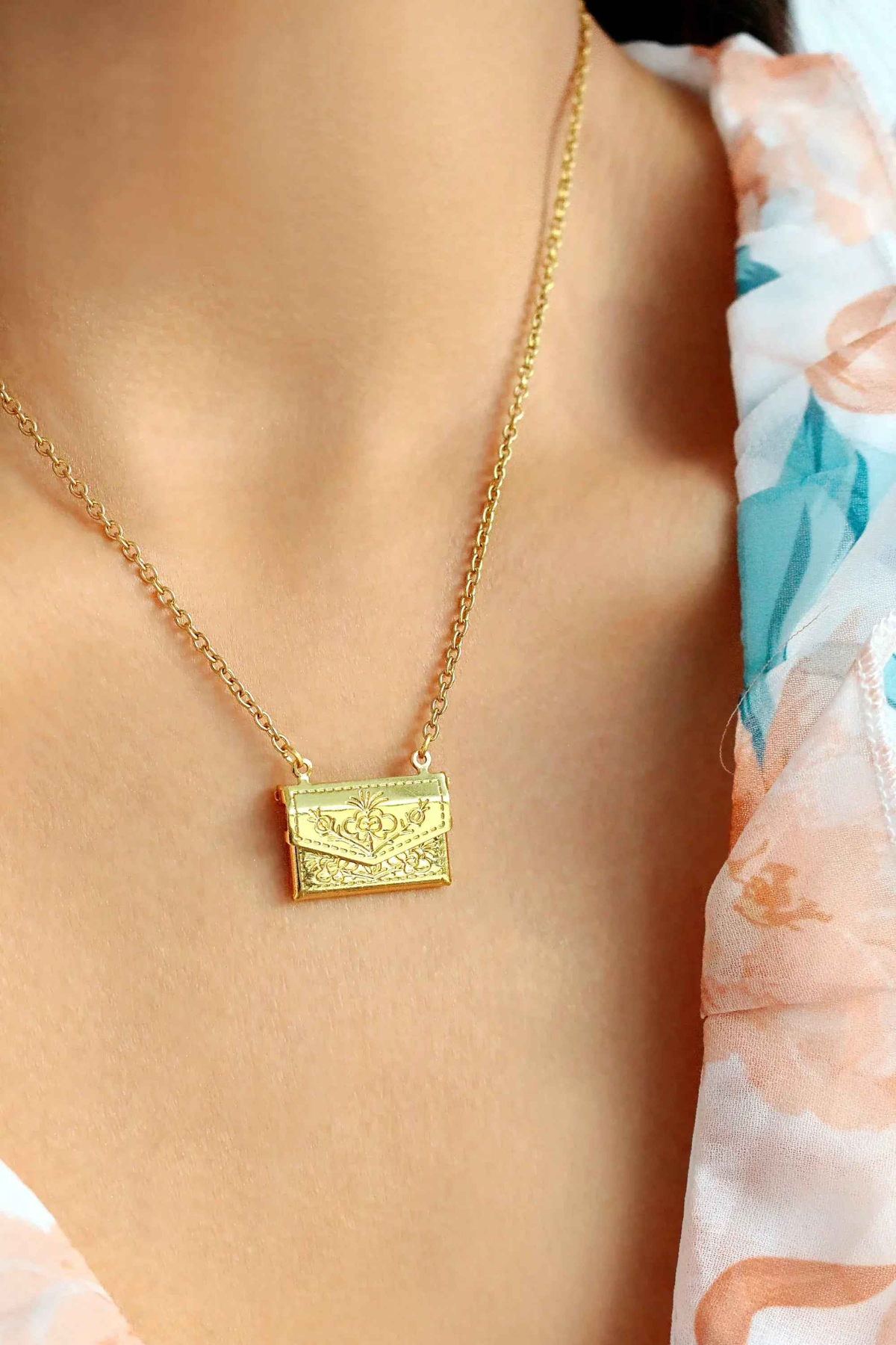 Gold envelope locket necklace with a delicate daisy engraving, displayed on a neutral background.
