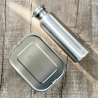 Zero waste starter kit with stainless steel bento-style lunchbox and water bottle on a wooden table.