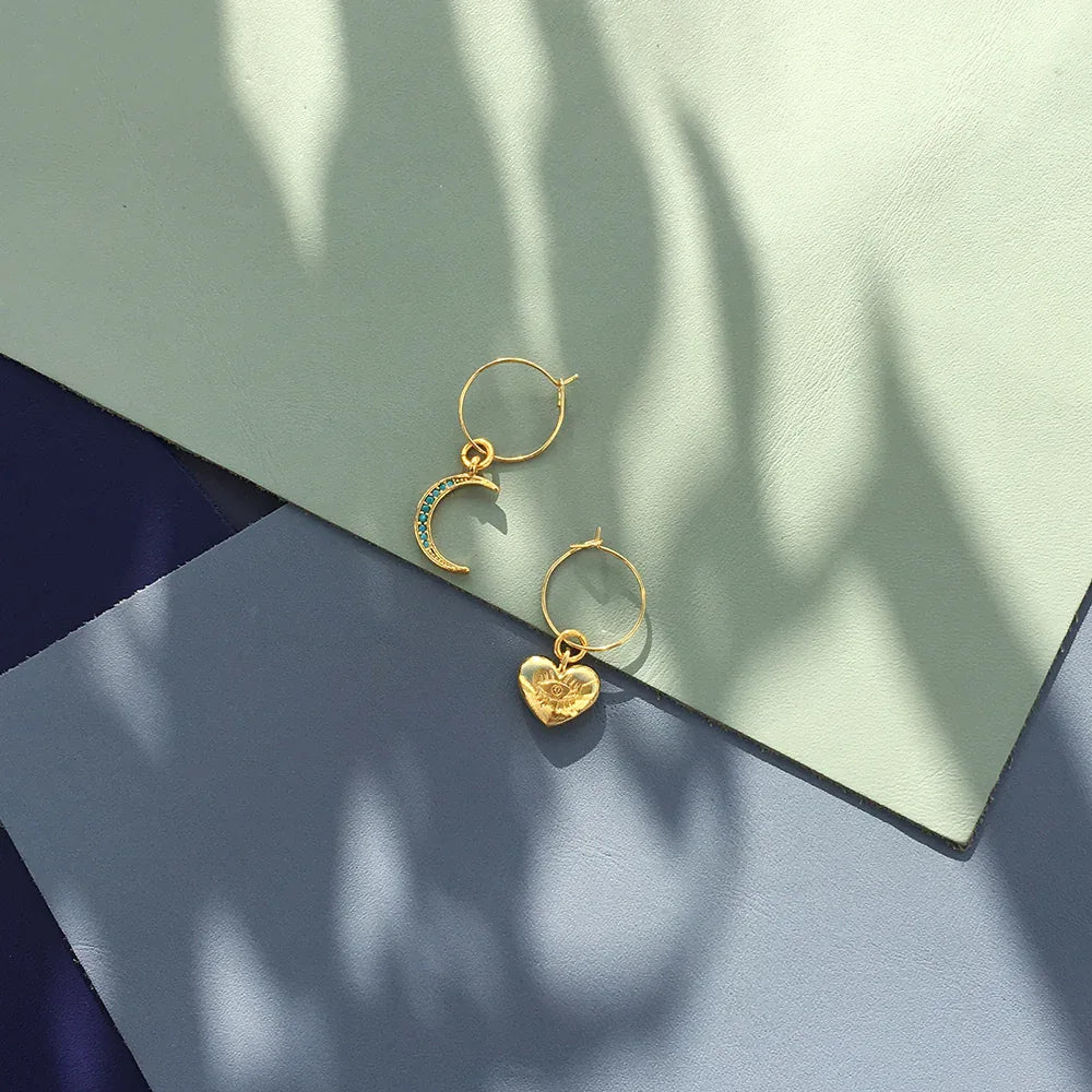 Model wearing turquoise crystal moon and gold heart charm mini hoop earrings.