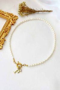 A delicate choker necklace with freshwater pearls and a gold-plated initial charm at the front opening.
