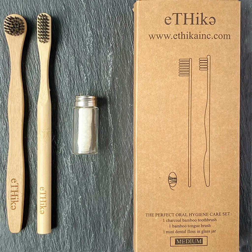 Bamboo toothbrush, tongue brush, and mint dental floss displayed neatly on wooden surface.