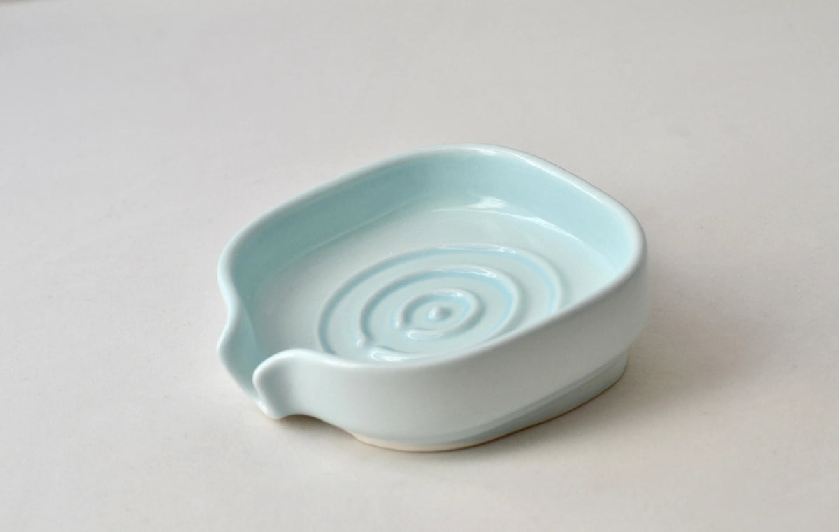 Stacked ceramic soap dishes in natural light highlighting smooth finish.